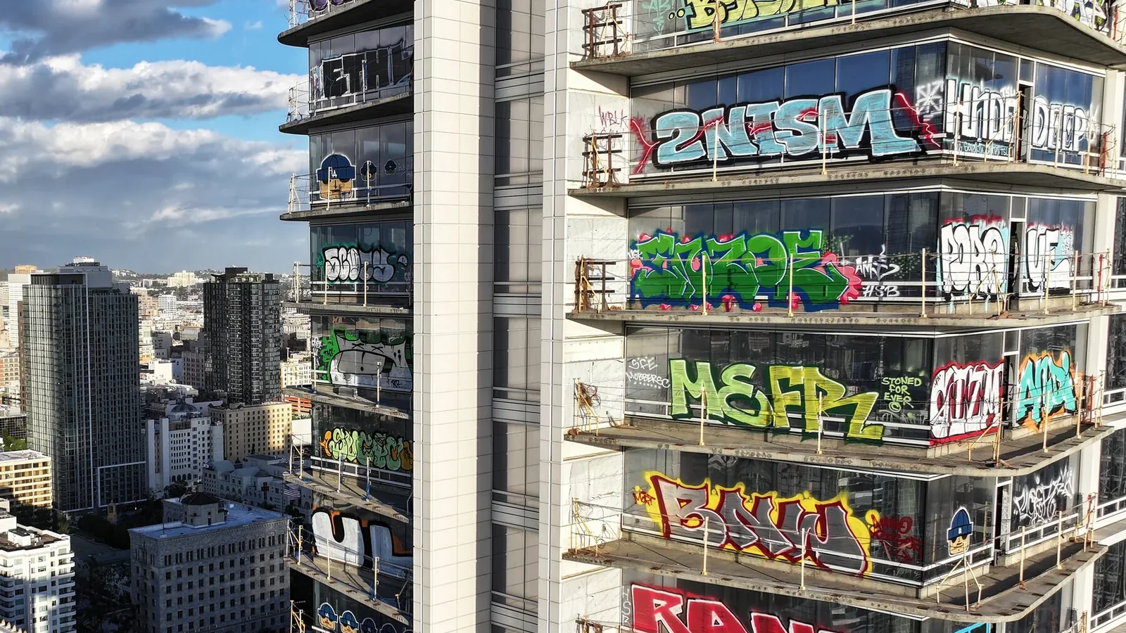 Two unfinished downtown Los Angeles towers, every floor covered in colourful graffiti, against a blue sky.